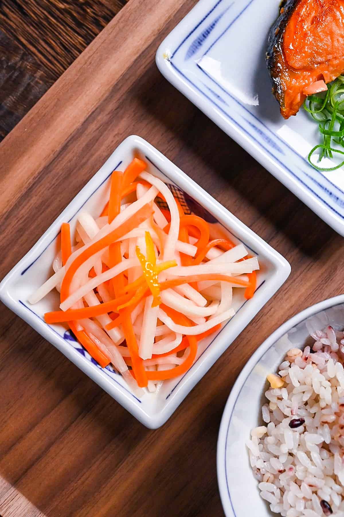 Kohaku namasu made with daikon and carrot served in a square white dish topped with yuzu peel