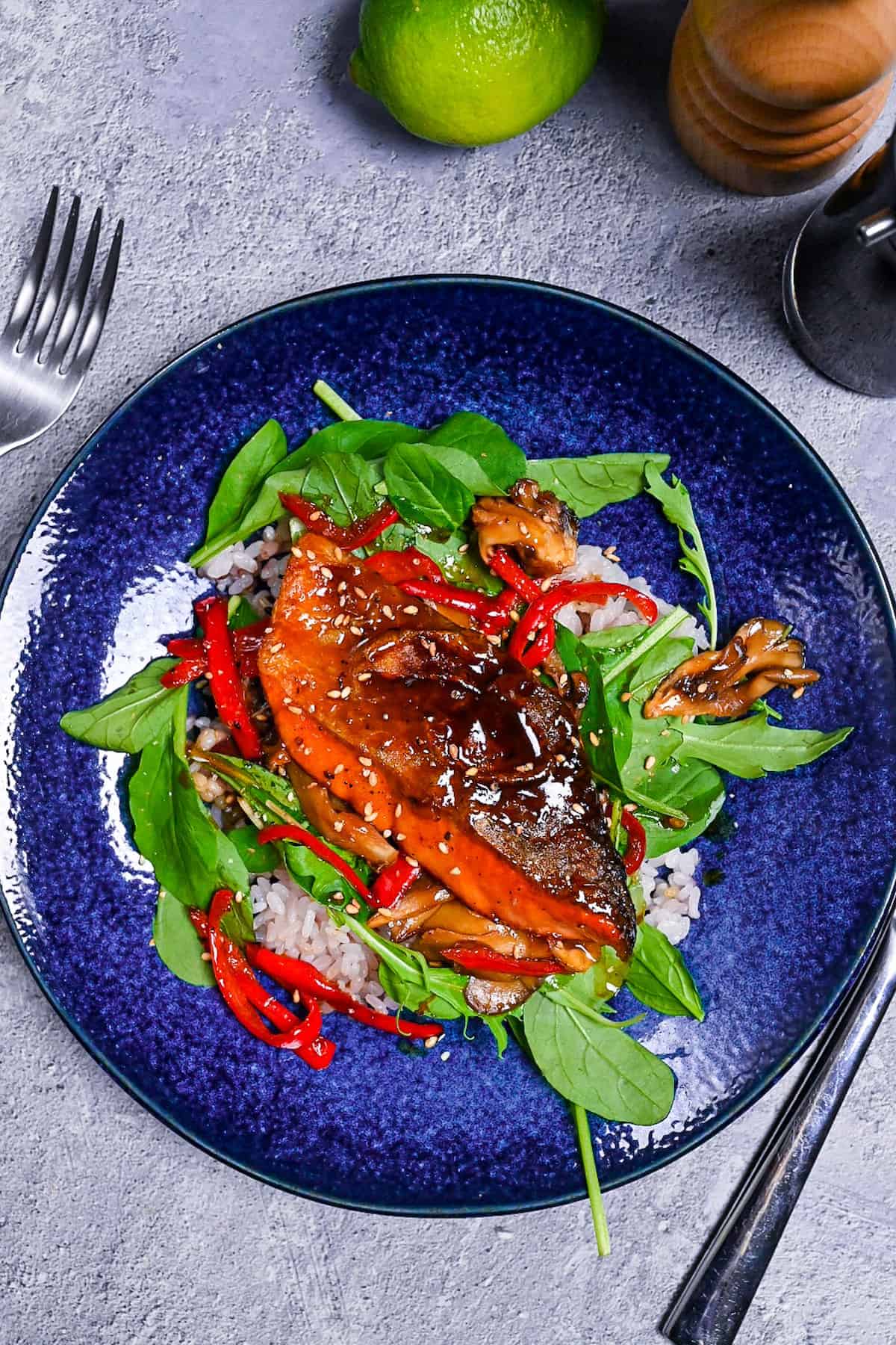 Ponzu salmon served with baby leaf, sautéed bell peppers and mushrooms over mixed grain rice on a blue plate
