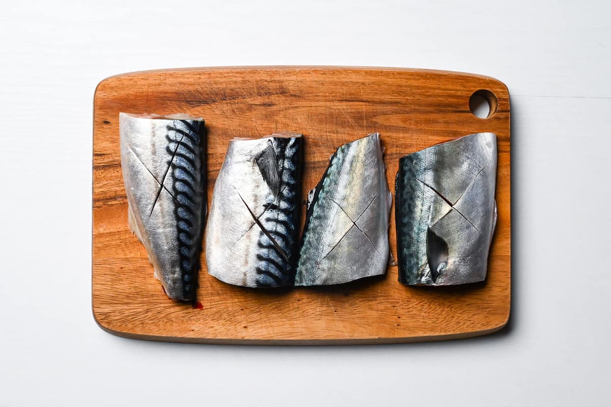 Scored mackerel fillets on a wooden chopping board