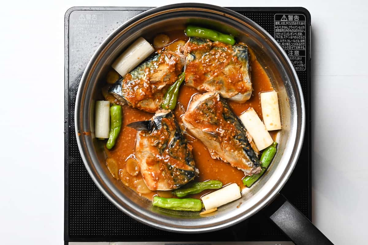 Miso mackerel simmering in a pan with shishito peppers and spring onion