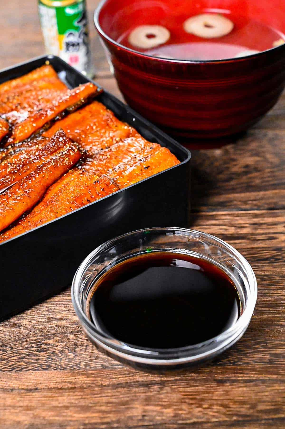 Unagi sauce in a small glass bowl next to grilled eel in a lacquerware box (unajyu)
