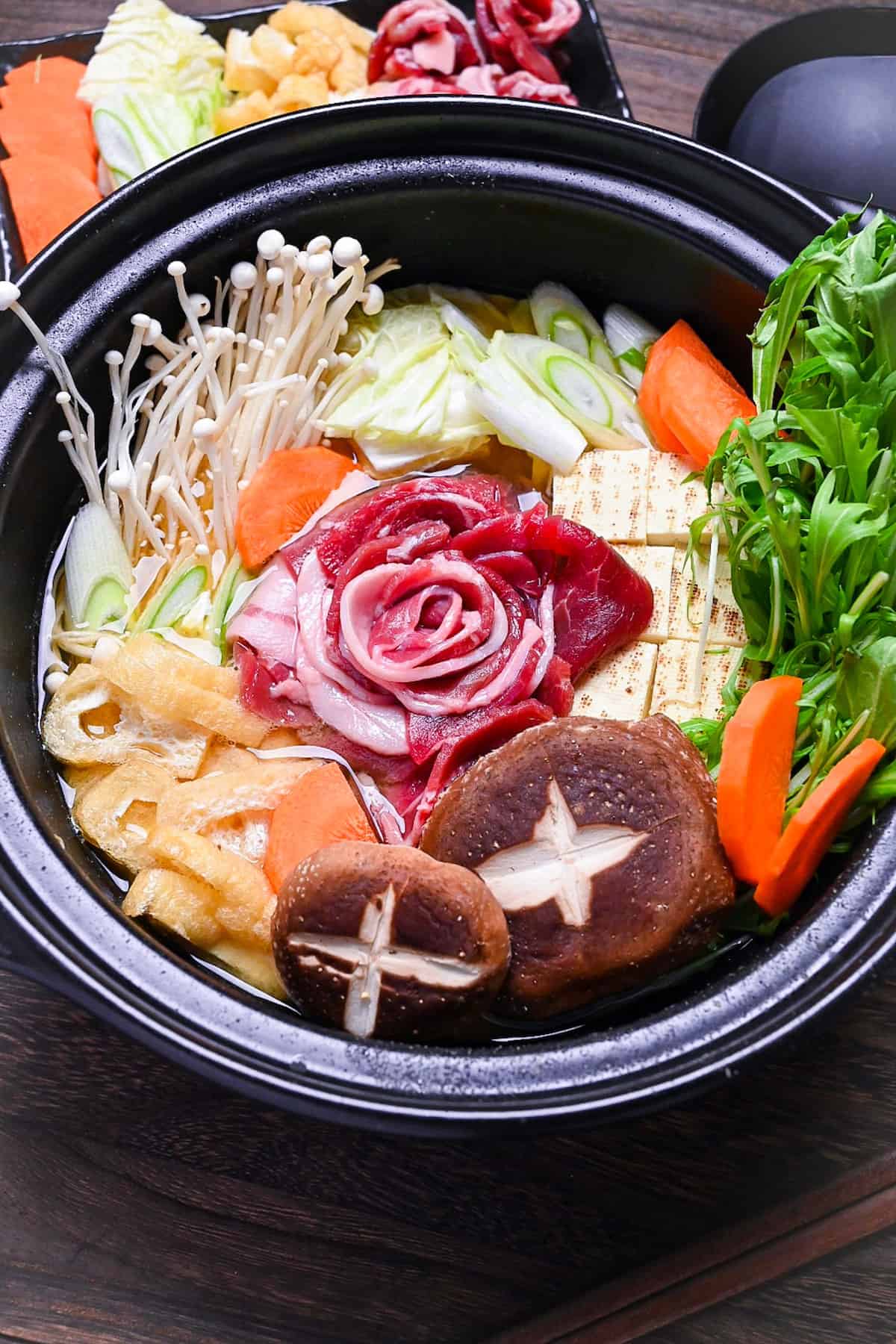 Botan nabe served in a black hot pot made with wild boar, tofu and vegetables in a miso flavoured broth