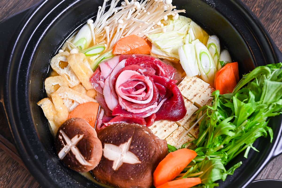 Botan nabe served in a black hot pot made with wild boar, tofu and vegetables in a miso flavoured broth