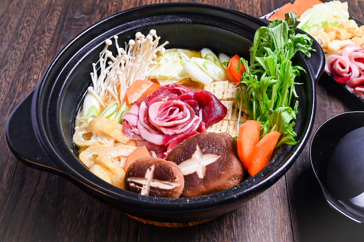 Botan nabe served in a black hot pot made with wild boar, tofu and vegetables in a miso flavoured broth