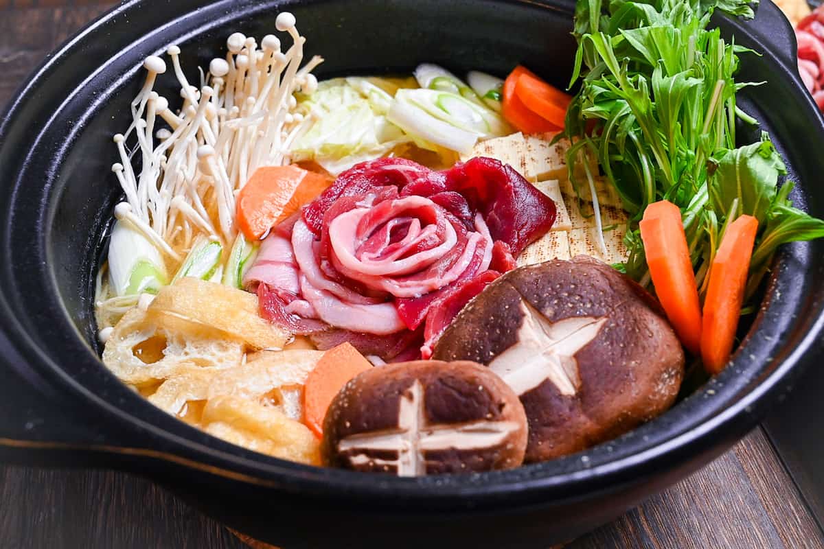 Botan nabe served in a black hot pot made with wild boar, tofu and vegetables in a miso flavoured broth