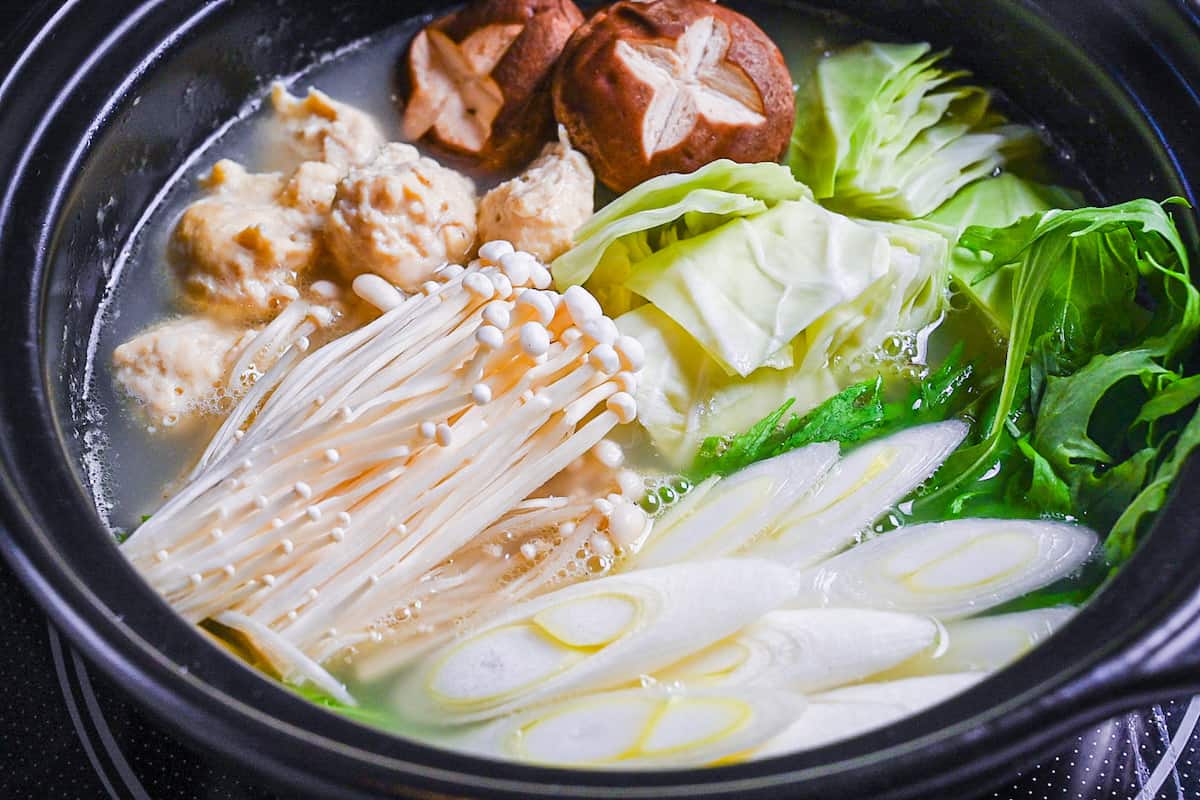 Hakata Chicken Mizutaki in a hot pot with homemade chicken meatballs, enoki, shiitake, cabbage, mizuna and spring onion in a rich chicken and kombu broth