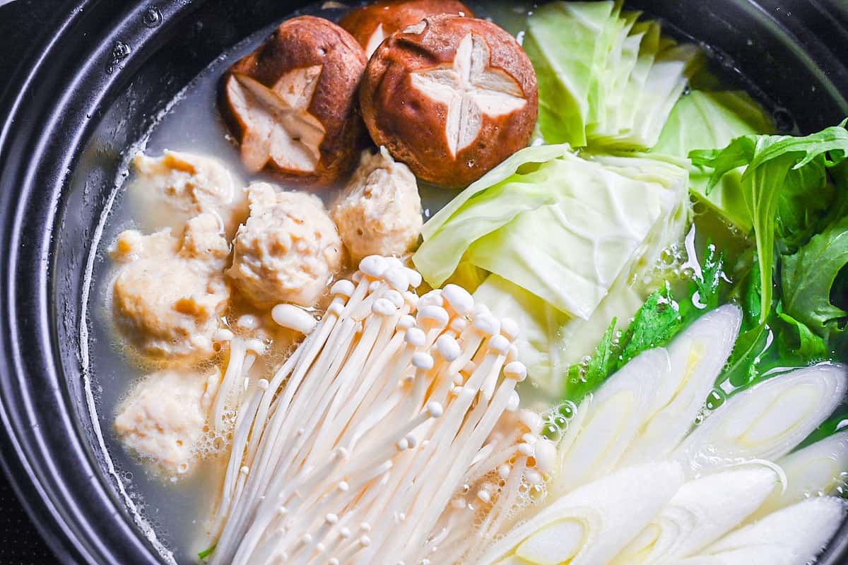 Hakata Chicken Mizutaki in a hot pot with homemade chicken meatballs, enoki, shiitake, cabbage, mizuna and spring onion in a rich chicken and kombu broth