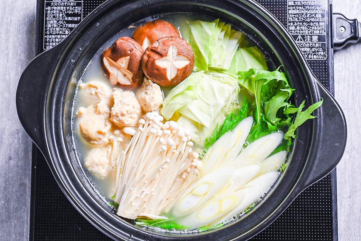 Hakata Chicken Mizutaki in a hot pot with homemade chicken meatballs, enoki, shiitake, cabbage, mizuna and spring onion in a rich chicken and kombu broth