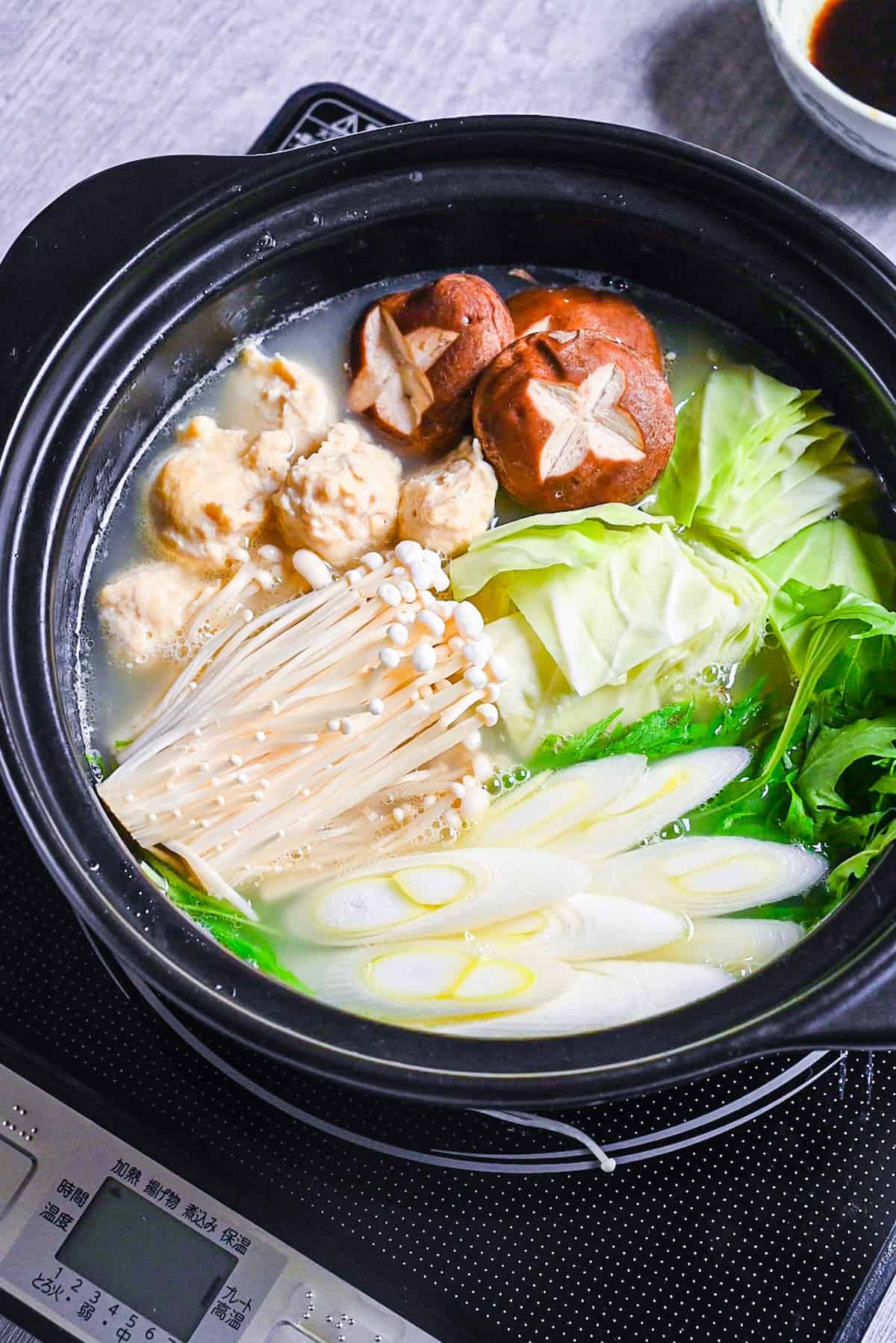 Hakata Chicken Mizutaki in a hot pot with homemade chicken meatballs, enoki, shiitake, cabbage, mizuna and spring onion in a rich chicken and kombu broth