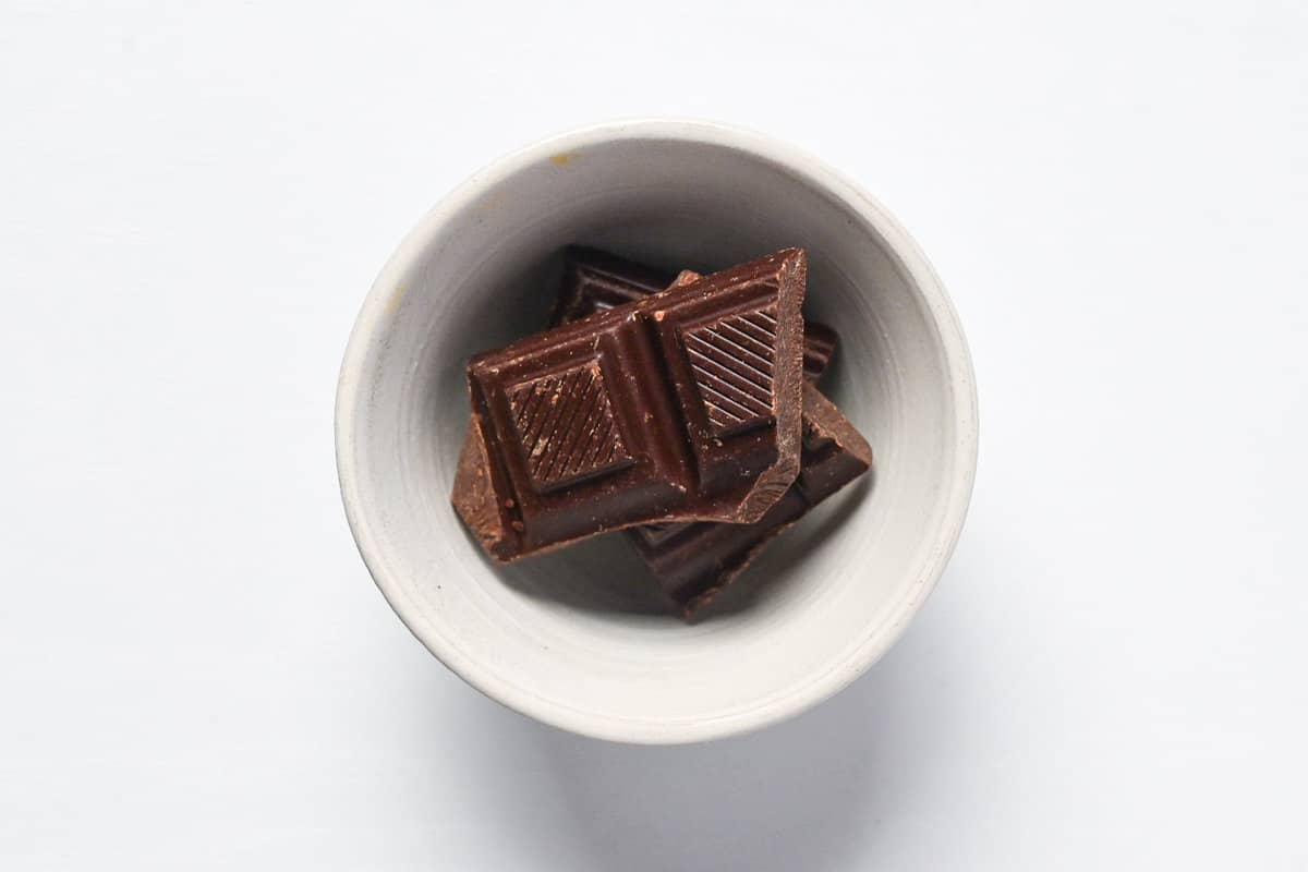 Broken pieces of dark chocolate in a small ceramic bowl