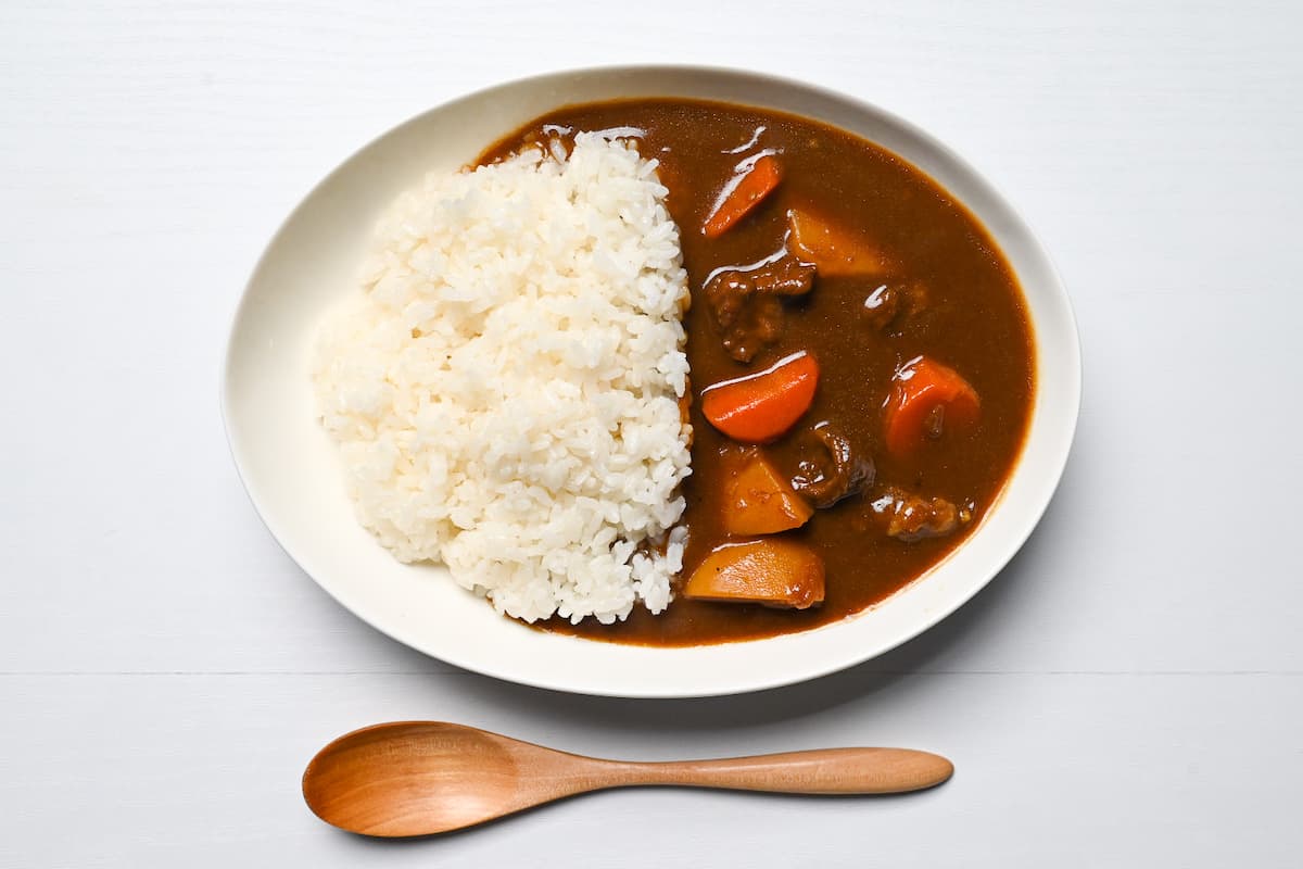Japanese curry made with curry roux, beef, carrots, onions and potatoes with white rice on a white plate