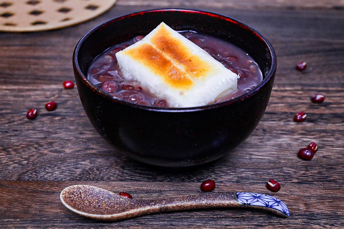 Zenzai (Japanese red bean soup) served in a black bowl and topped with toasted kirimochi