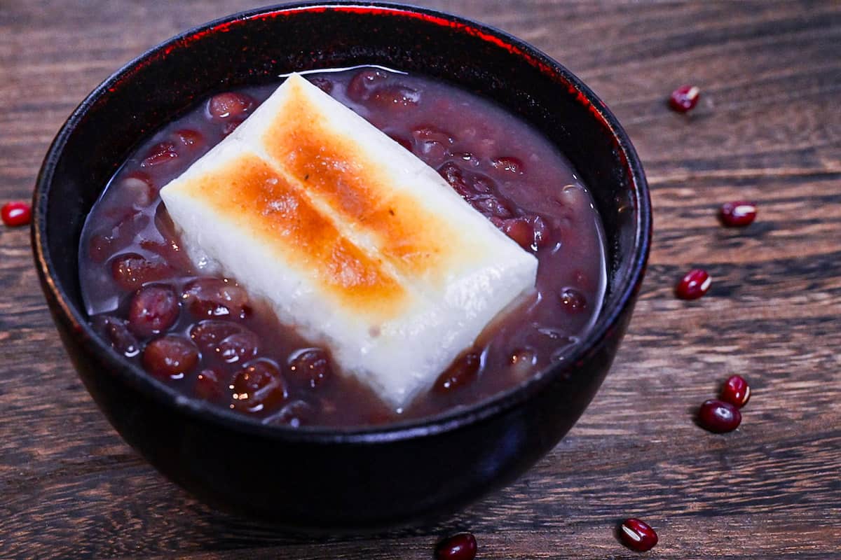 Zenzai (Japanese red bean soup) served in a black bowl and topped with toasted kirimochi
