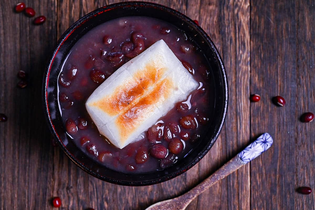 Zenzai (Japanese red bean soup) served in a black bowl and topped with toasted kirimochi
