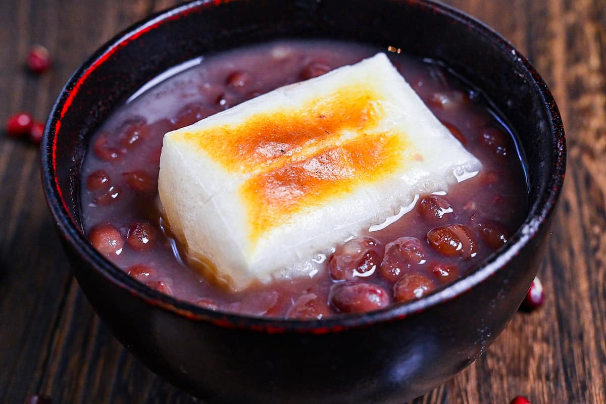 Zenzai (Japanese red bean soup) served in a black bowl and topped with toasted kirimochi