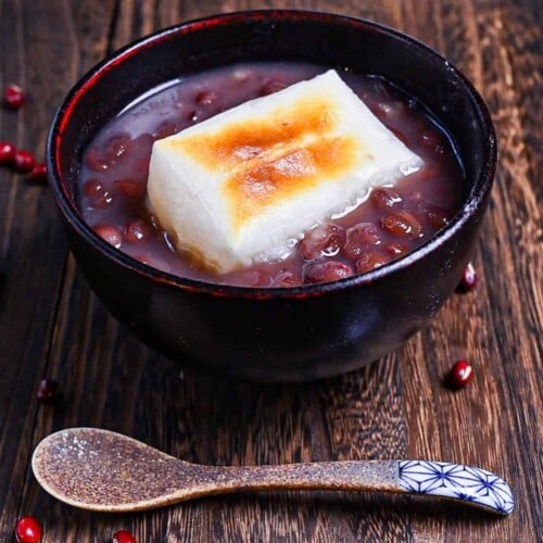 Zenzai (Japanese red bean soup) served in a black bowl and topped with toasted kirimochi