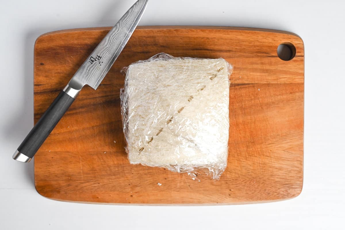Ichigo sando wrapped with plastic wrap and marked with a guideline for cutting placed on a wooden chopping board
