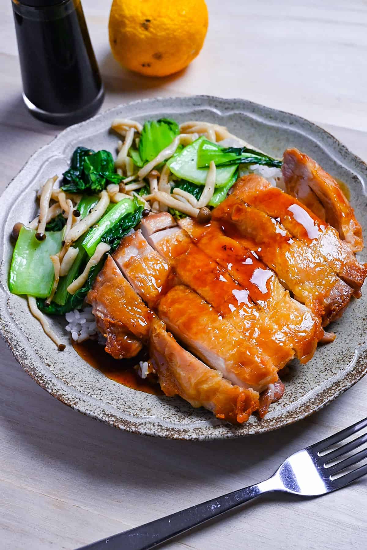 Crispy chicken steak drizzled with ponzu sauce served with rice and sautéed vegetables on a beige plate