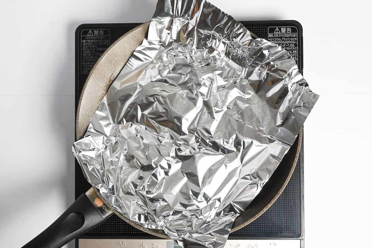 chicken thighs in a frying pan covered with foil