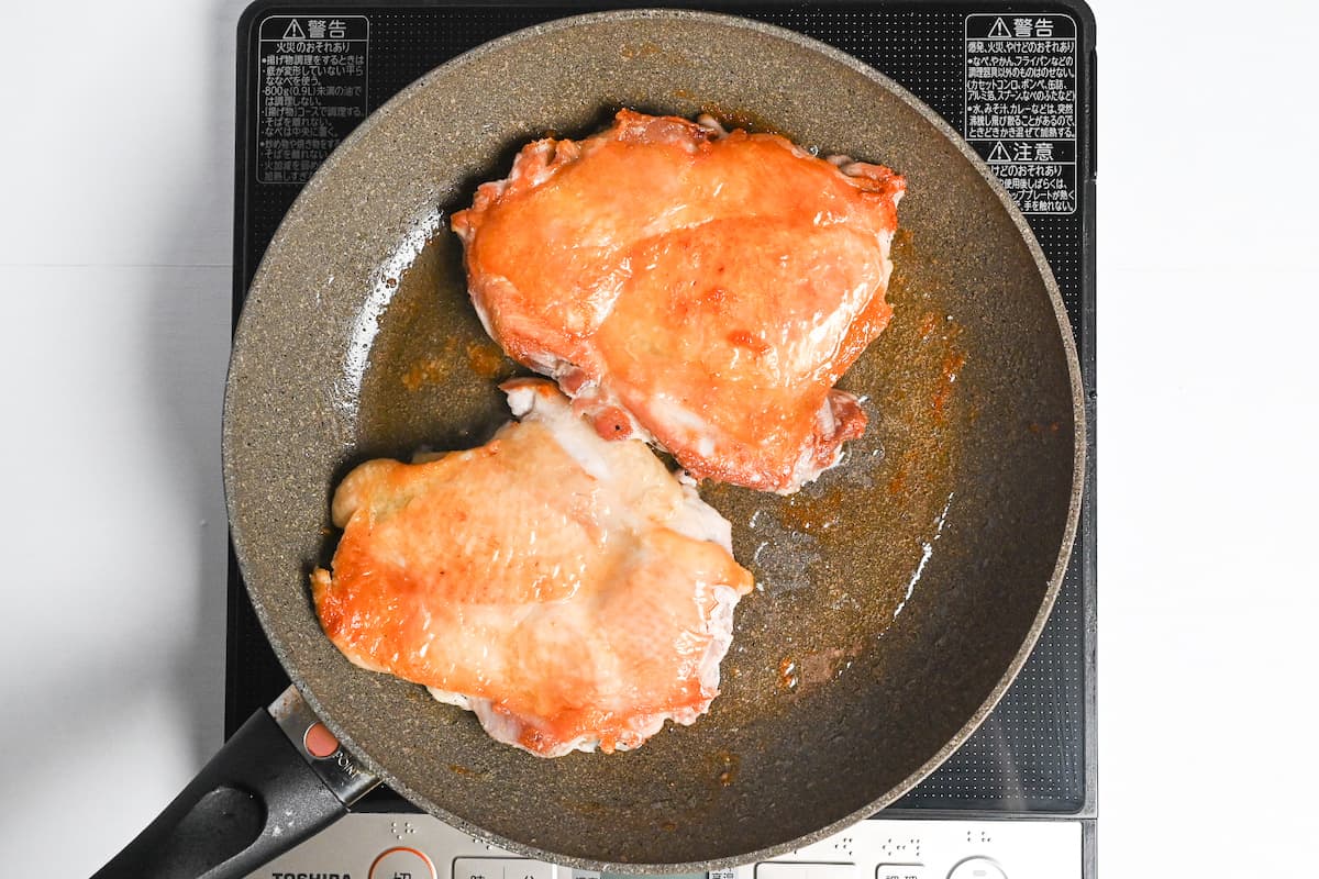 chicken thighs with crispy skin frying in a large pan