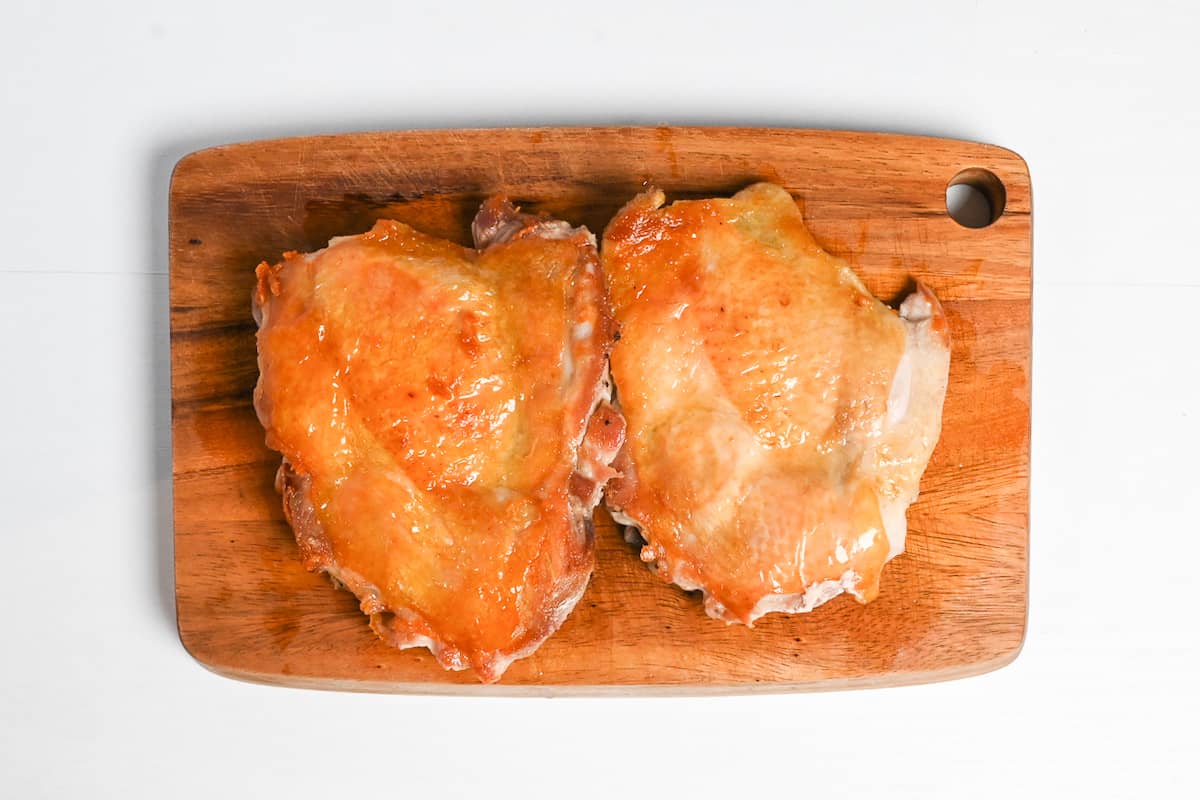 Crispy skin-on chicken thighs resting on a wooden chopping board
