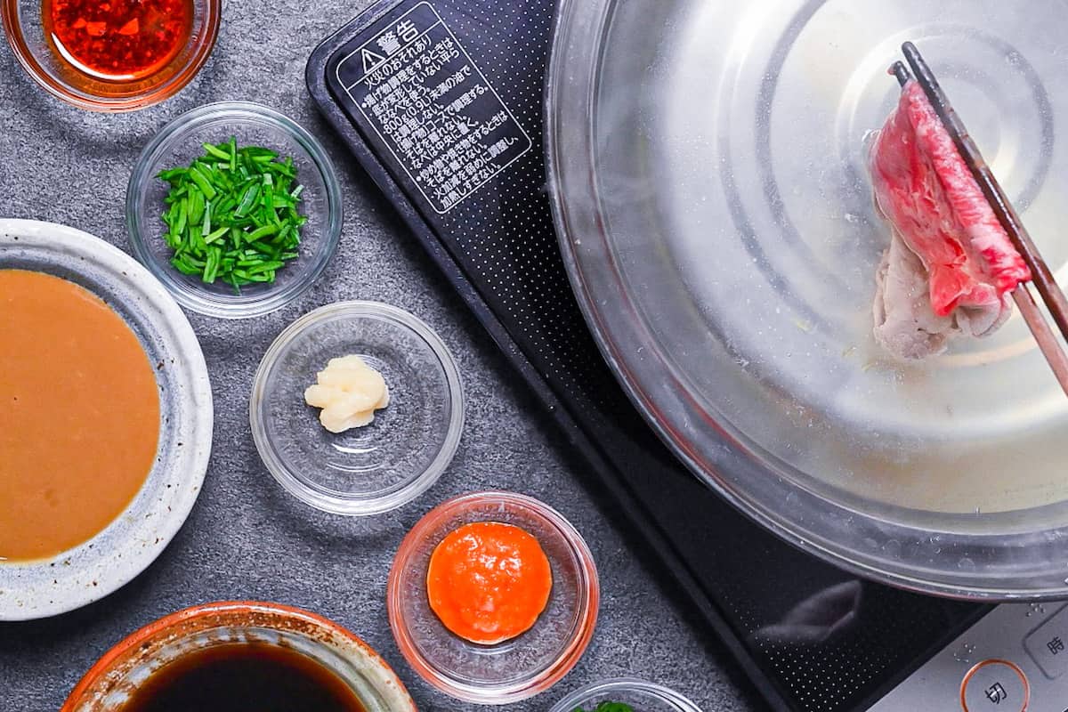 Swishing thinly sliced wagyu beef in a kombu and yuzu dashi broth next to shabu shabu dipping sauces and additional condiments