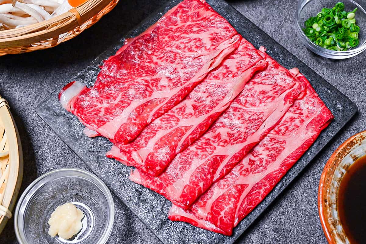 Thinly sliced cuts of wagyu beef for shabu shabu on a black square plate