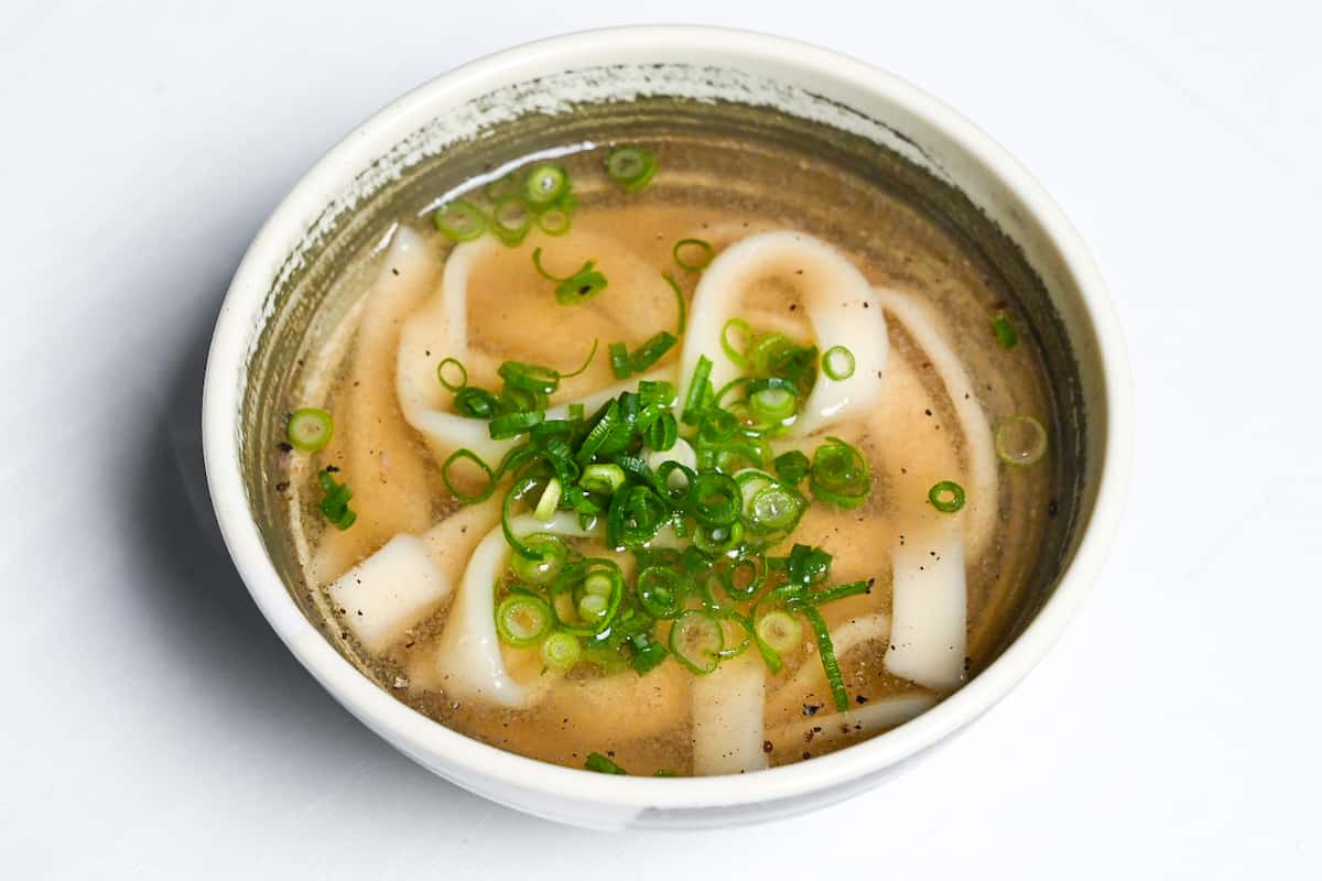 A single portion of kishimen noodles served in shabu shabu broth topped with chopped spring onion.