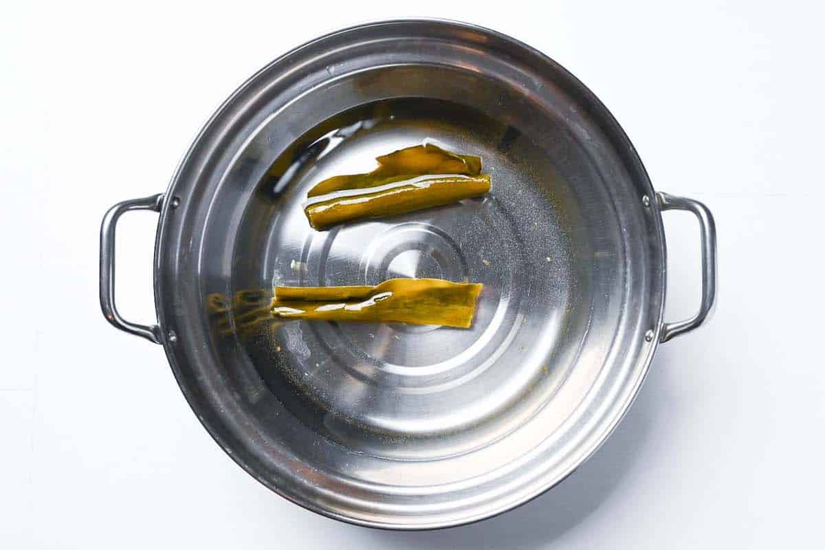 Two pieces of kombu soaking in an aluminum pot