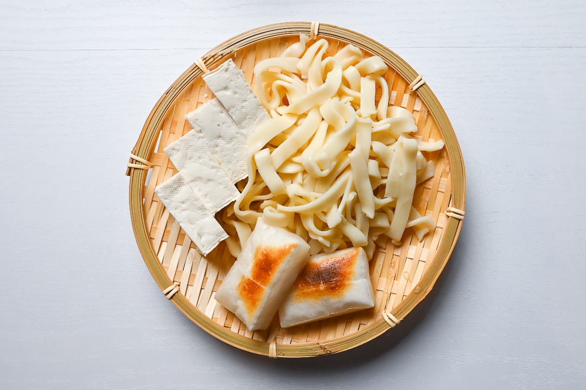 Tofu, kishimen noodles (flat udon) and toasted mochi rice cakes arrange on a bamboo zaru