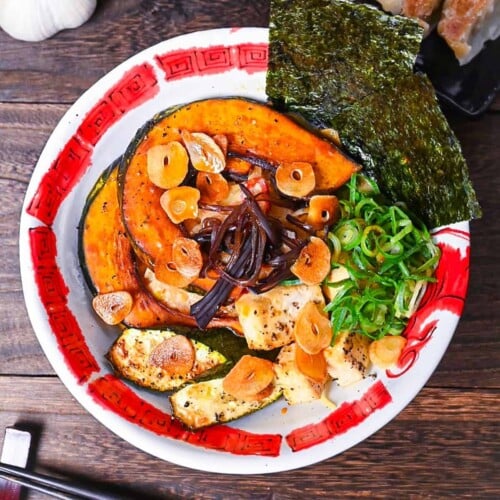 Spicy vegetarian miso ramen topped with oven baked kabocha, tofu and zucchini in a red and white bowl
