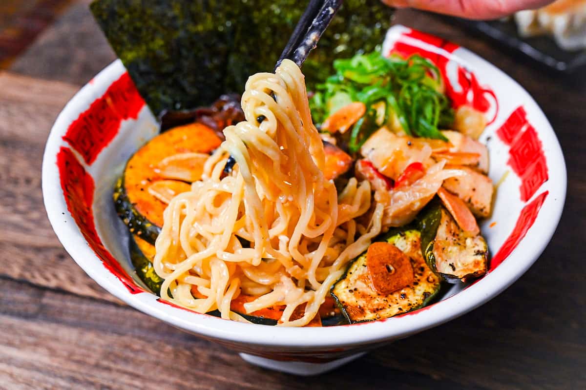 Spicy vegetarian miso ramen topped with oven baked kabocha, tofu and zucchini in a red and white bowl