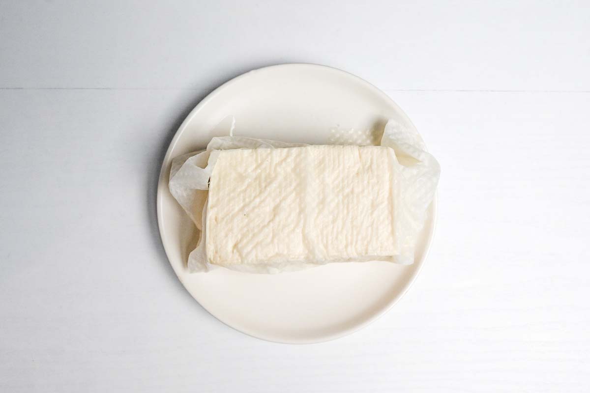 Tofu wrapped in kitchen paper on a white plate