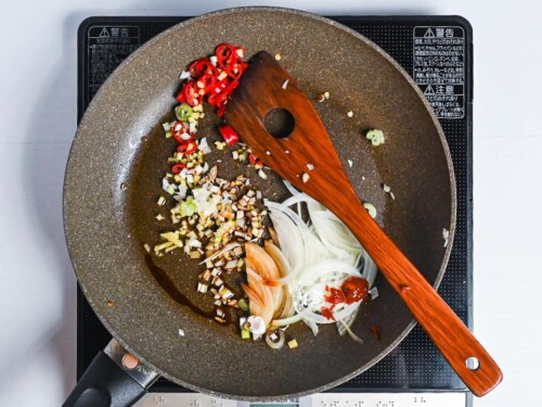 Chili, spring onion, ginger and white onion frying in a pan with condiments
