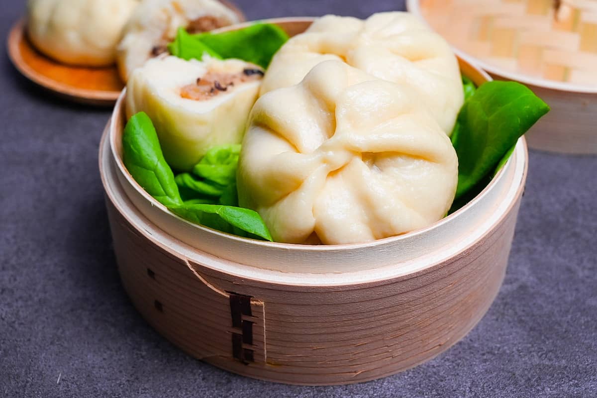 Japanese "nikuman" steamed pork buns in a bamboo steamer arranged over green frilly lettuce side view