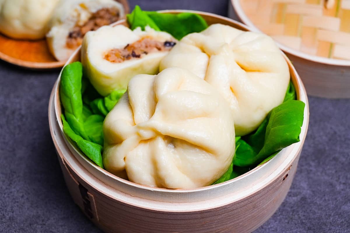 Japanese "nikuman" steamed pork buns in a bamboo steamer arranged over green frilly lettuce side view