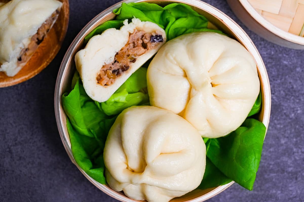 Japanese "nikuman" steamed pork buns in a bamboo steamer arranged over green frilly lettuce top down