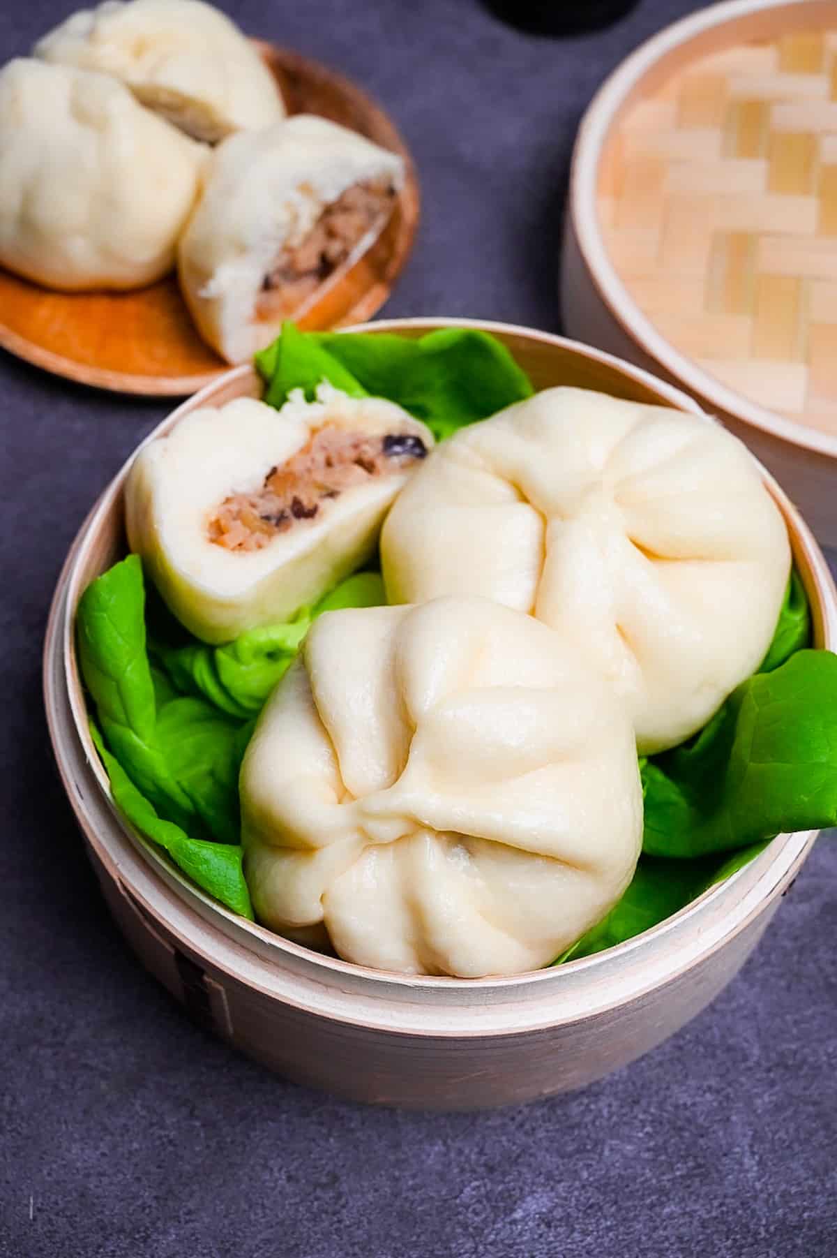 Japanese "nikuman" steamed pork buns in a bamboo steamer arranged over green frilly lettuce