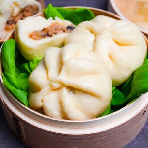 Japanese "nikuman" steamed pork buns in a bamboo steamer arranged over green frilly lettuce