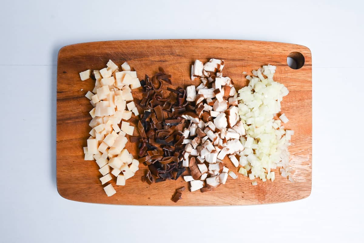 Finely diced bamboo shoot, wood ear mushroom, shiitake mushroom and onion on a wooden chopping board