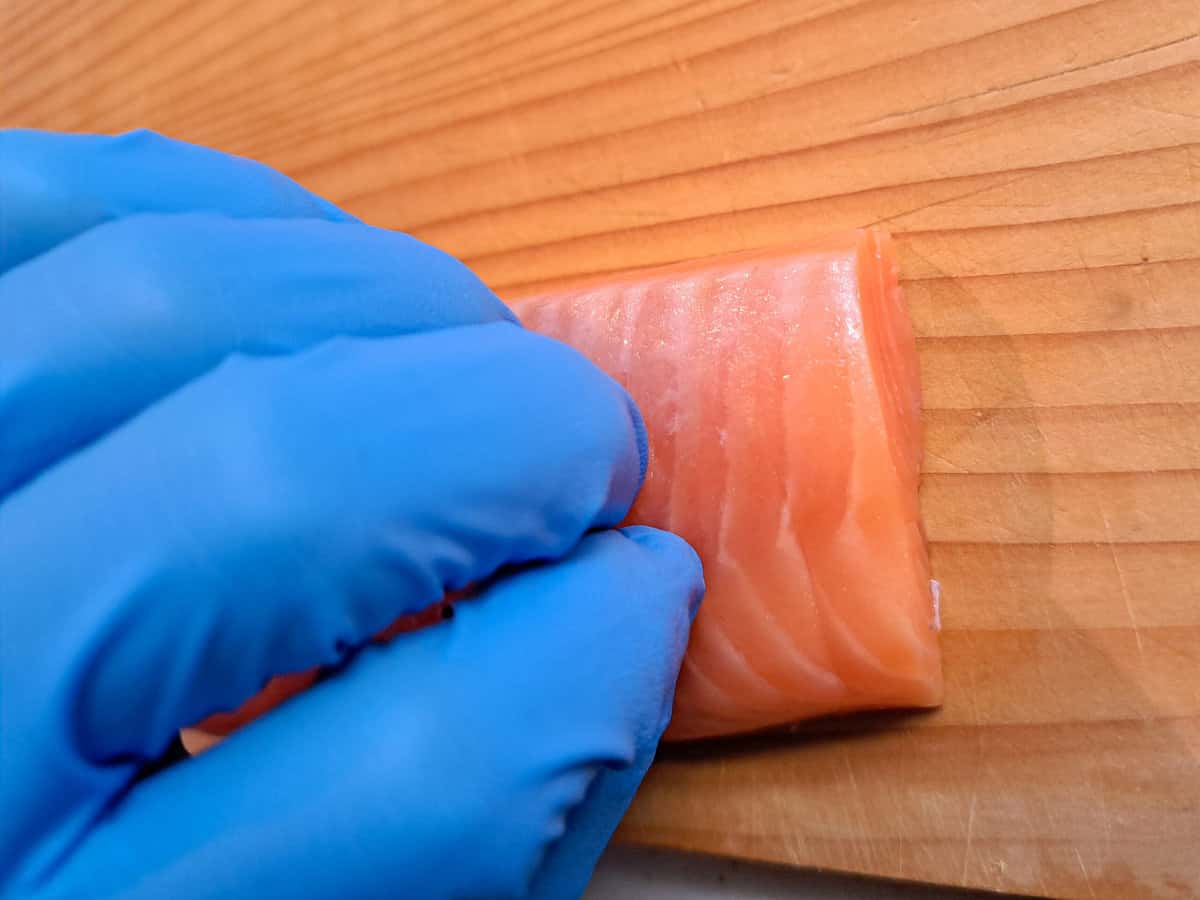 The left hand presses down on the salmon with fingers bent.