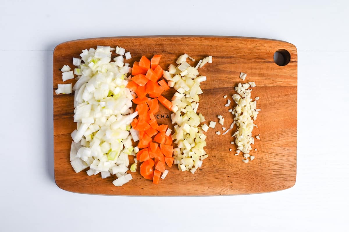 Diced onion, carrot and celery on a wooden chopping board with finely diced garlic