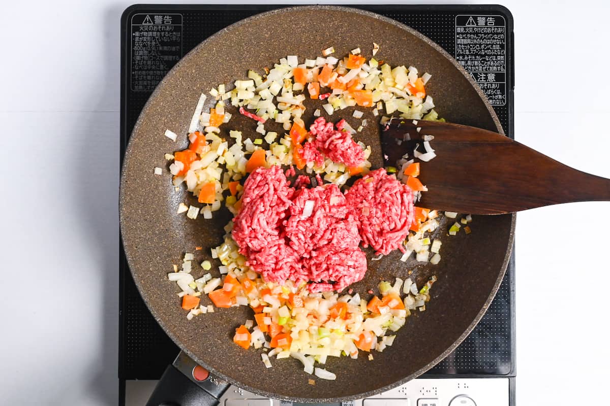 Ground beef added to a pan of softened onion, carrots and celery