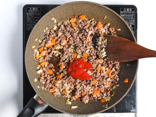 Ketchup and condiments added to cooked ground beef and vegetables in a large frying pan