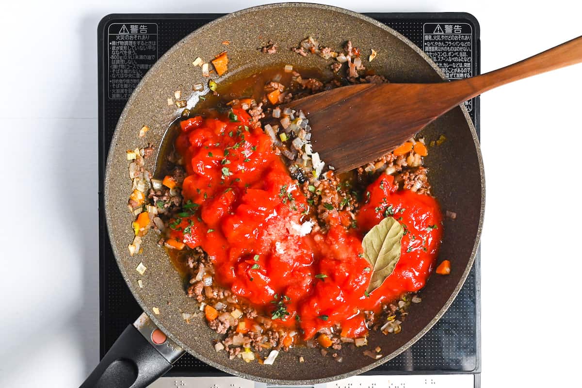 Canned tomatoes, sugar and bay leaf added to the pan for spaghetti meat sauce