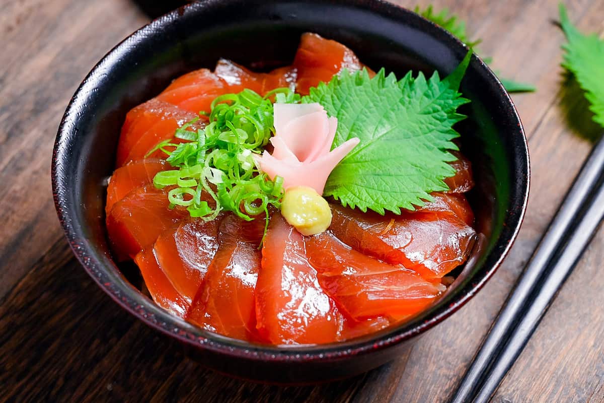 Tekkadon - vinegared rice topped with slices of fresh tuna sashimi, pickled ginger, wasabi, shiso and chopped spring onion in a black lacquerware bowl