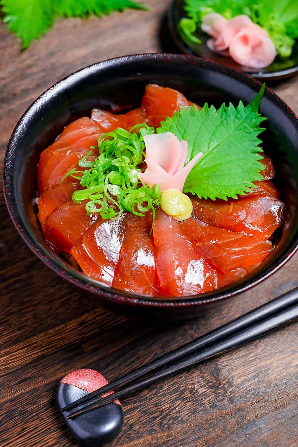 Tekkadon - vinegared rice topped with slices of fresh tuna sashimi, pickled ginger, wasabi, shiso and chopped spring onion in a black lacquerware bowl