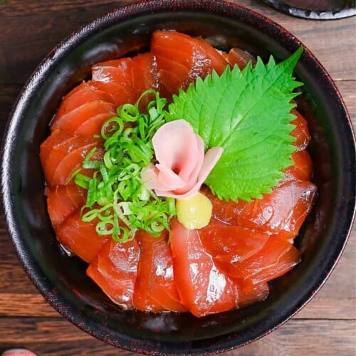 Tekkadon - vinegared rice topped with slices of fresh tuna sashimi, pickled ginger, wasabi, shiso and chopped spring onion in a black lacquerware bowl