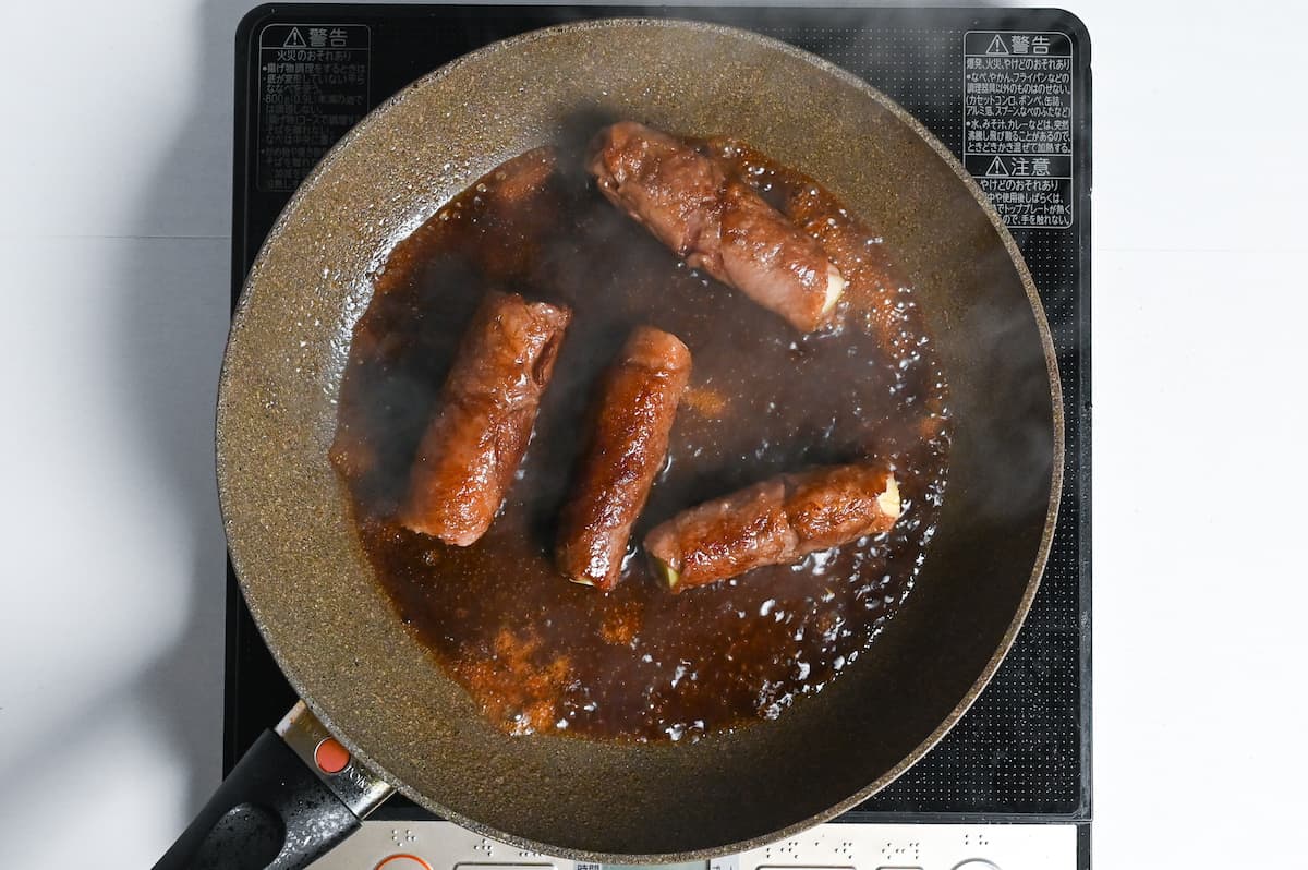 beef negimaki frying in sauce in a frying pan