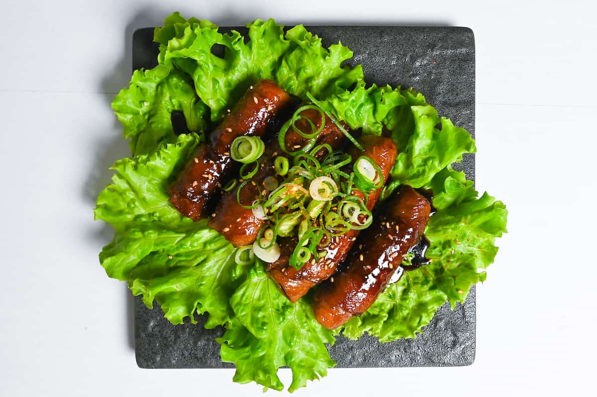 Japanese beef negimaki served over a bed of frilly lettuce and topped with chopped spring onions and sesame seeds